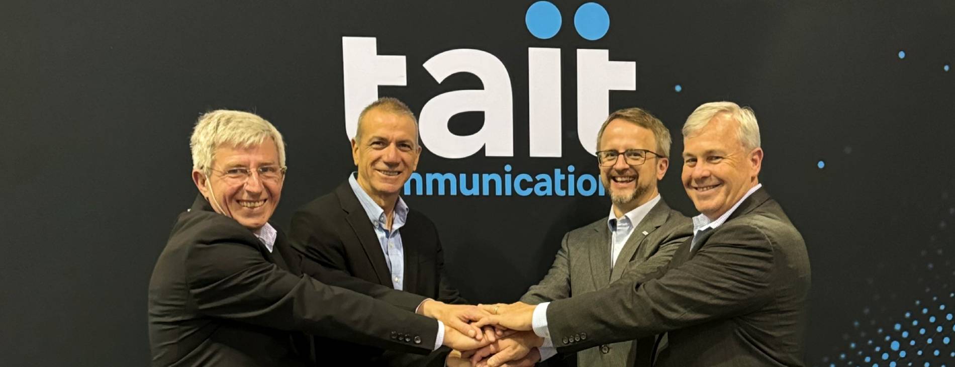 Four business men from Frequentis and Tait shaking hands