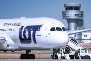 an airplane of the polish airlines LOT infront of an airport tower