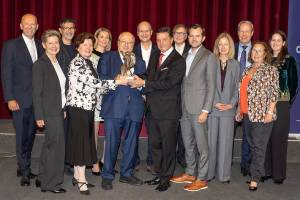 a festive group with mr. bardach in the middle holding the award statue