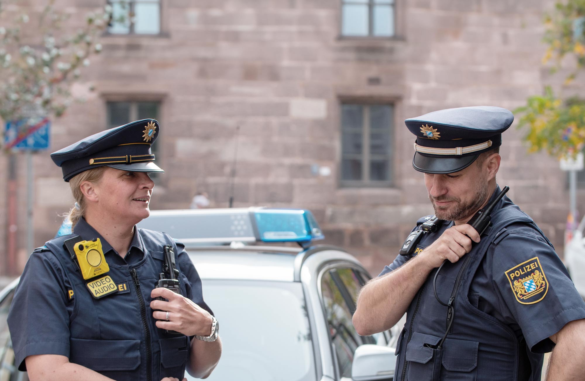 Police forces header picture, showing a male and a female person in uniform, police car in the background