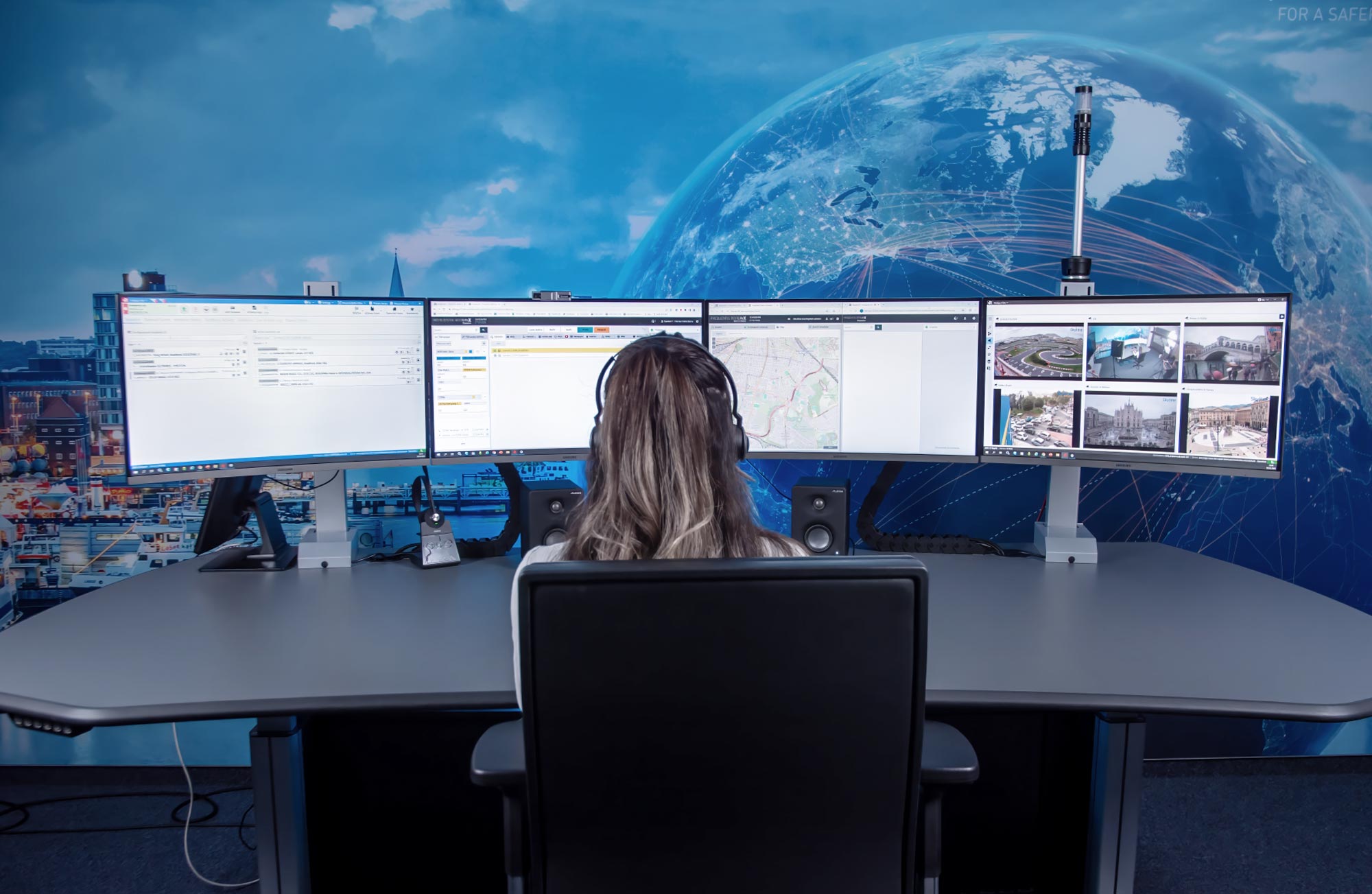 Unified Communications website header, showing a woman sitting in a control room, in front of four screens