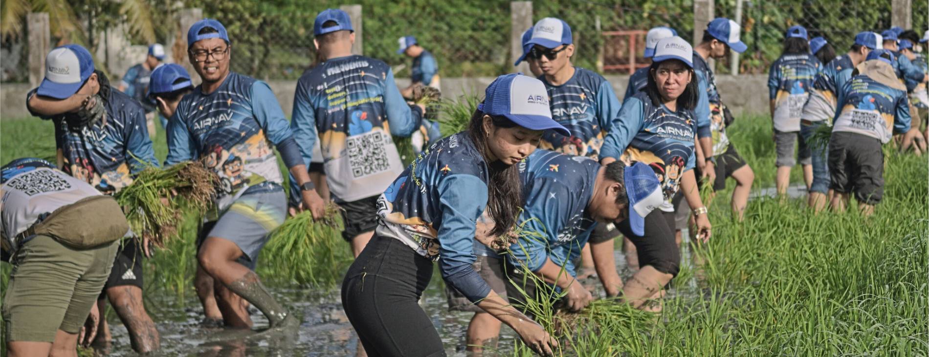 Frauen und Männer mit AirNav-T-Shirts und -Kapperln in einem Reisfeld