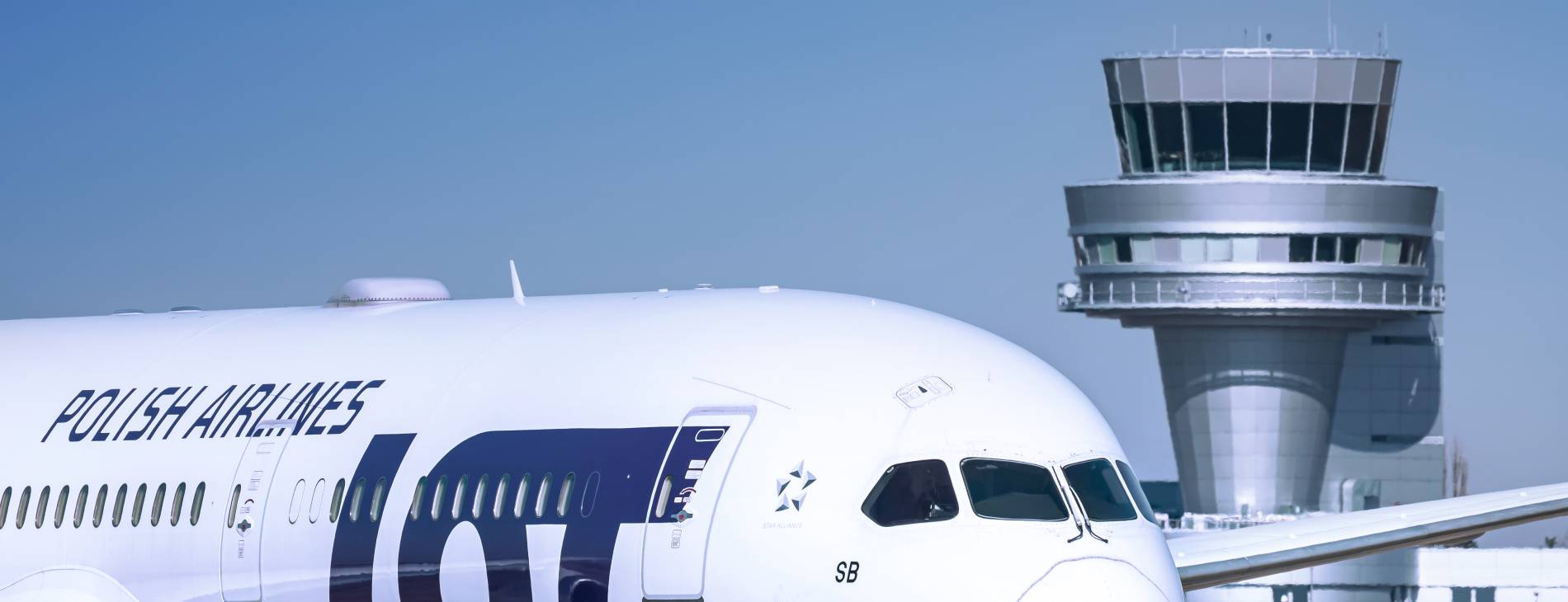 an airplane of the polish airlines LOT infront of an airport tower