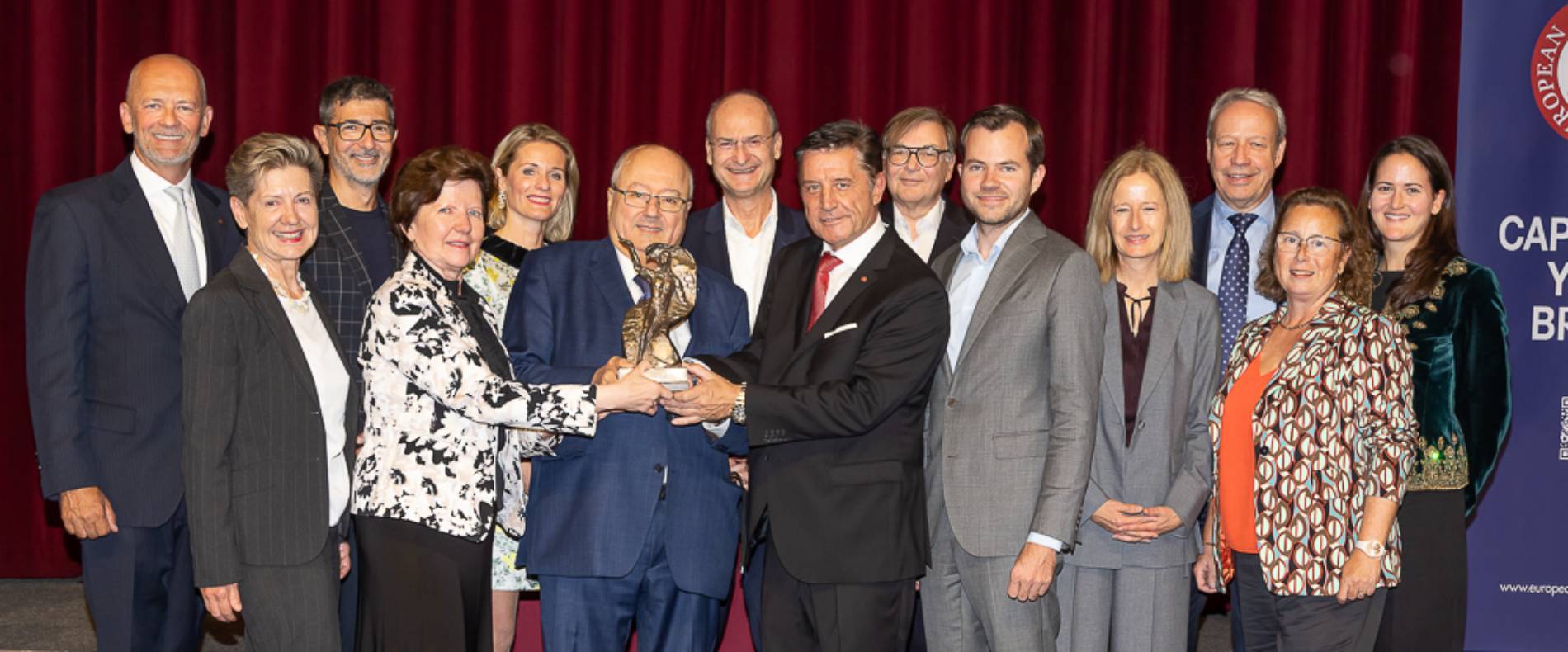 a festive group with mr. bardach in the middle holding the award statue